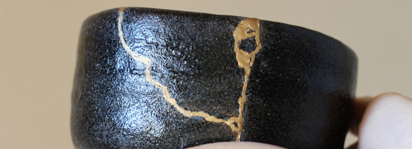 Hände, die eine mit Kintsugi reparierte Schüssel halten. 