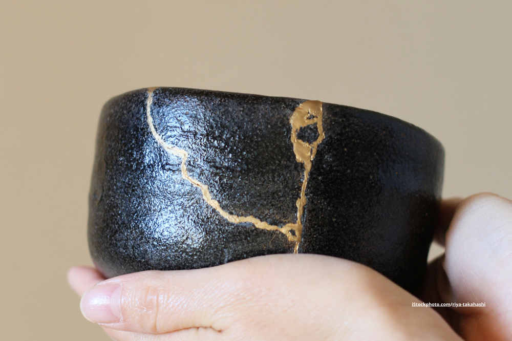 Hände, die eine mit Kintsugi reparierte Schüssel halten. 