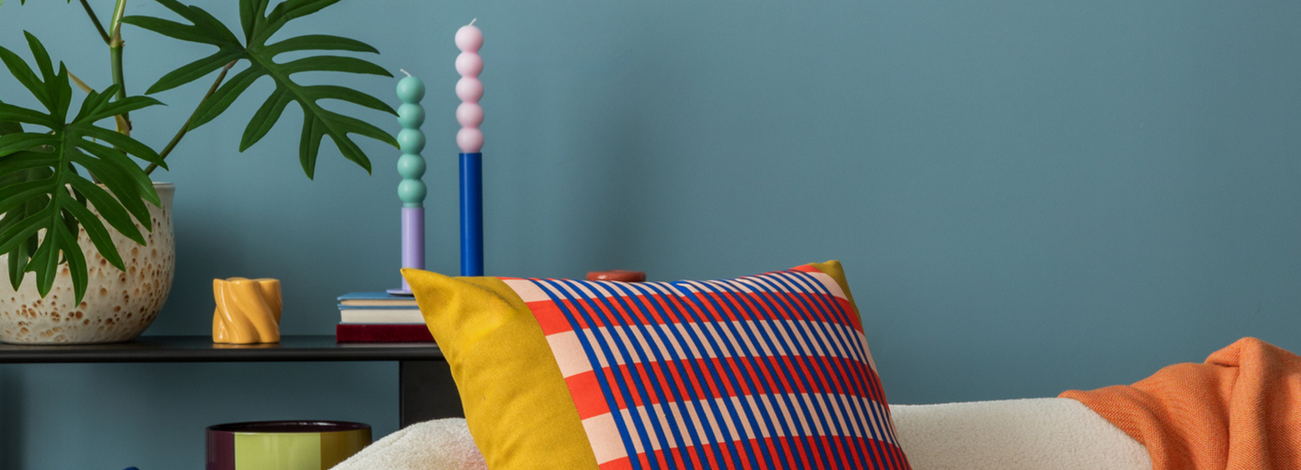 Ein Sofa mit bunten Kissen und weitere farbenfrohe Dekoelemente. Die Wand ist blau. 