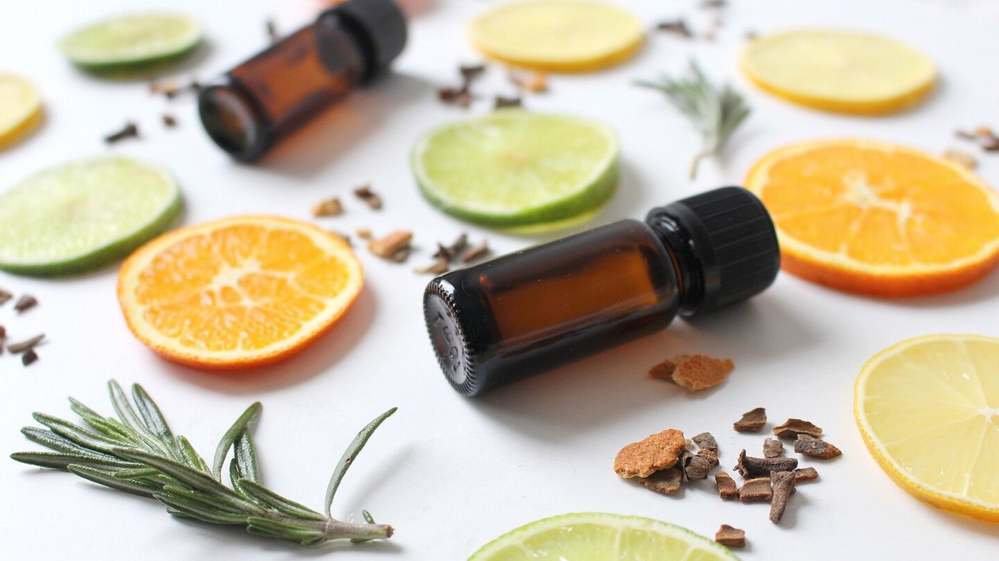 Das Foto zeigt zwei Flaschen ätherischer Öle und Orangen- und Limettenscheiben.