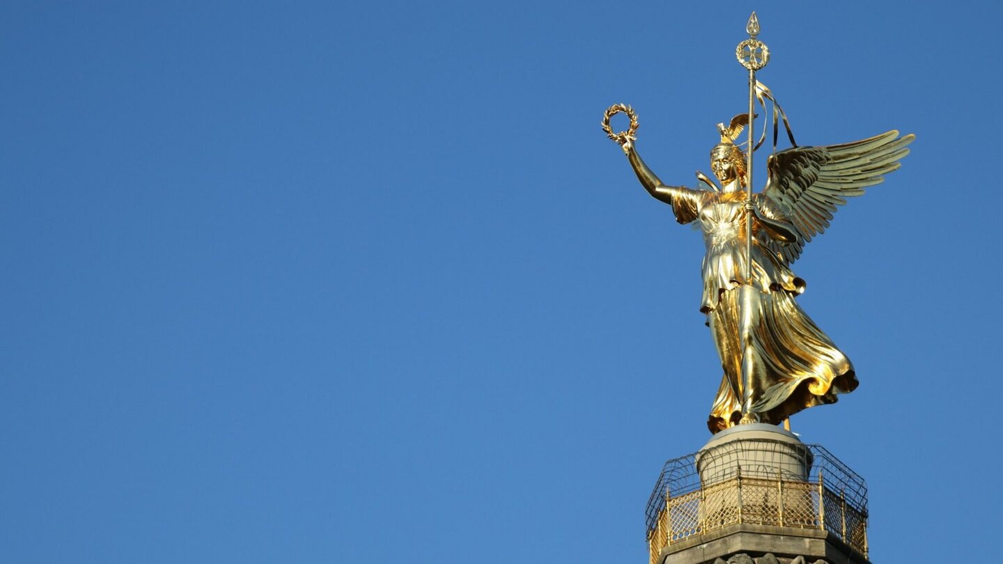 Die Siegessäule in Berlin mit der goldenen Viktoria-Statue, die stolz in den klaren blauen Himmel ragt.