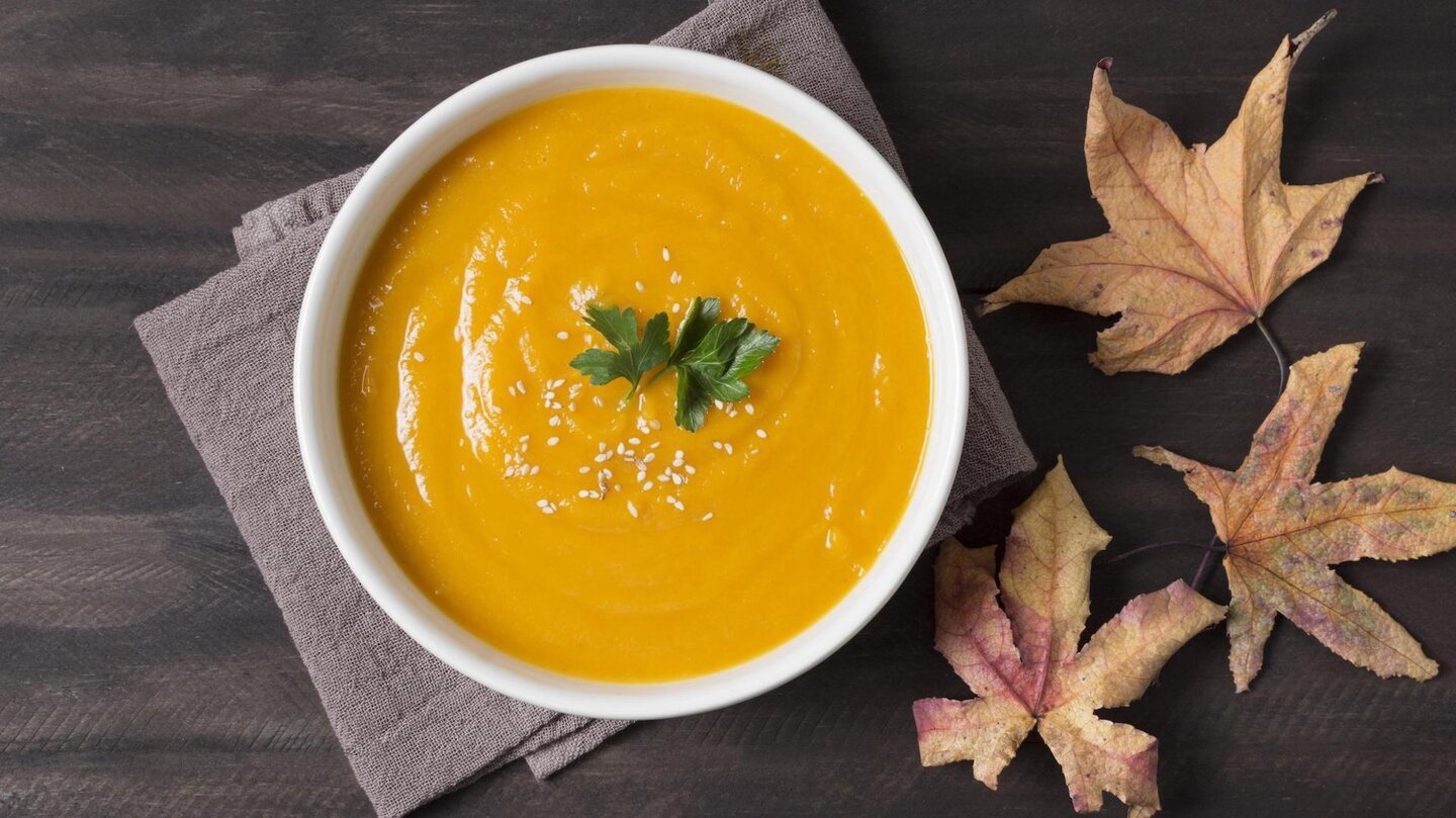 Das Foto zeigt eine Schale Kürbissuppe vor herbstlicher Dekoration.